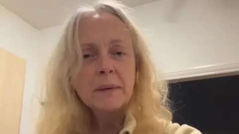 A woman in her 50s with blonde hair looks at the camera