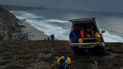 St Agnes Coastguard A coastguard van with equipment visible on a cliff with three people approaching.