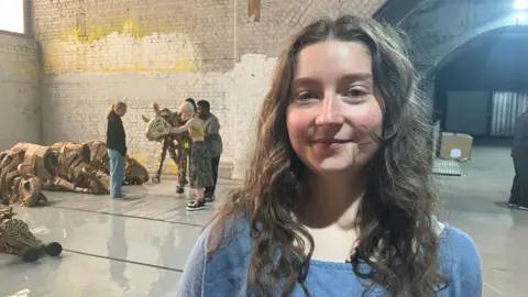 Photograph of Eva Greeves in front of animal puppets  