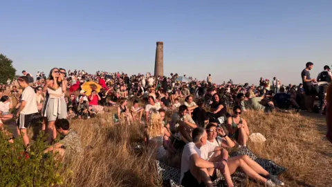 Handout Many people are sat and stood on a large hill to watch the eclipse
