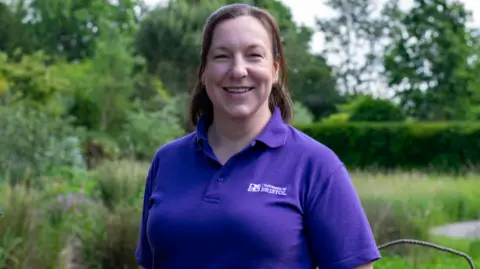 Caroline Rudge Caroline Rudge smiles into the camera wearing a purple top with the University of Bristol on it, with a garden backdrop behind her