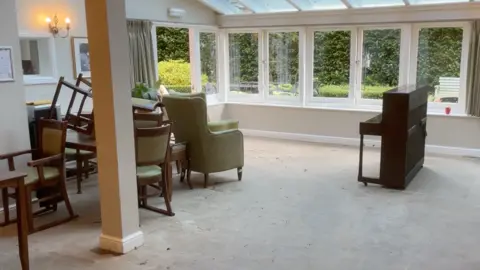 The ground floor of the care home with a piano, chairs and windows