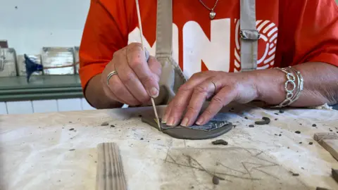 A close-up of Linda's hands cutting up some clay by hand on a cloth on a table.