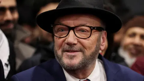 Reuters George Galloway, wearing a black hat and black glasses, looks past the camera while surrounded by smiling supporters in the background