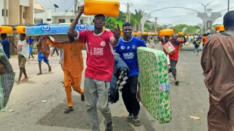  Zaharadeen Lawal / BBC People carrying away cartons full of vegetable cooking oil and mattresses in Kano, Nigeria - 1 August 2024