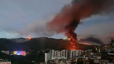 AFP via Getty Images Fire at Fuerte Tiuna, Venezuela's largest military complex, is seen from a distance.