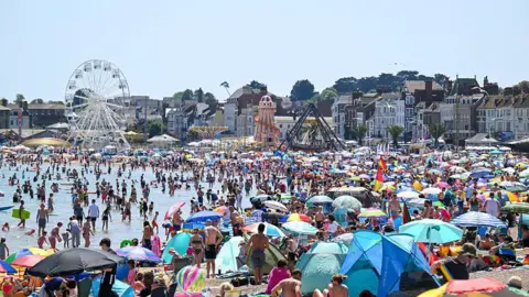 A general view of Weymouth beach during a heatwave in May, with hundreds of people using the beach and a blue sky above. 