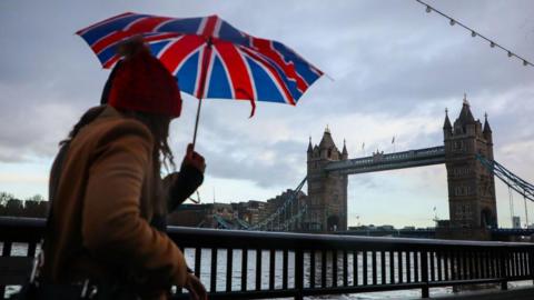 Woman carrying a Union Jack printed umbrella walking towards Tower Bridge in London