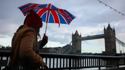 Getty Images Woman carrying a Union Jack printed umbrella walking towards Tower Bridge in London