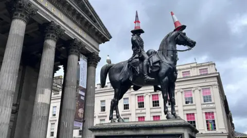 Duke of Wellington statue in Glasgow. It is a man sitting on a horse. There are orange traffic cones on the man's head and the horse's head.