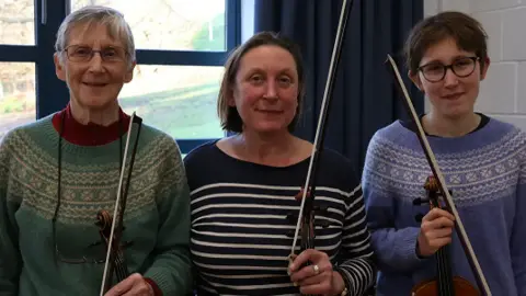 Marlborough Concert Orchestra Miranda Wilson, Anna Wilson and Astrid Wilson-Gignoux holding their violins and smiling
