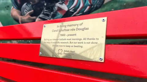 A golden plaque on a bright red bench