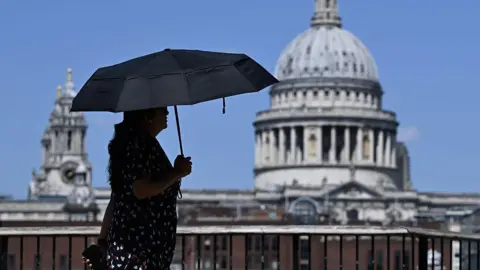 Getty Images A woman walks under an umbrella past St Paul's Cathedral in London during the heatwave.