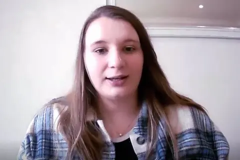 Learner driver Teddy, speaking via Zoom, with long brain hair and a checkered shirt