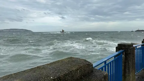 Choppy seas in Douglas Bay with the Tower of Refuge in the distance. There are blue railings in the fore.