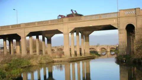 A stone viaduct above a river. Its reflection can be seen in the water. 