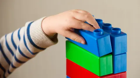 PA Media Child's hand playing with colourful building blocks