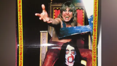 Other A man with fangs (Ozzy Osbourne) and wild hair reaches out from a throne, while a second man with white face paint and blood around his mouth sits below.
