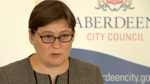 Angela Scott, a woman with glasses and short brown hair, in front of a backdrop that says Aberdeen City Council
