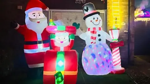 Jason Fletcher A colourful outdoor Christmas display with an inflatable Santa, snowman, and a smaller Santa popping out of a present.