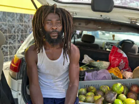 Brandon Drenon / BBC Local farmer Oreth Jones sits in the trunk of his car next to the last of his harvest