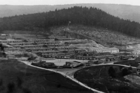 National Archive On a stark hillside are rows of long huts arranged in formidable structures, designed to prevent escape.