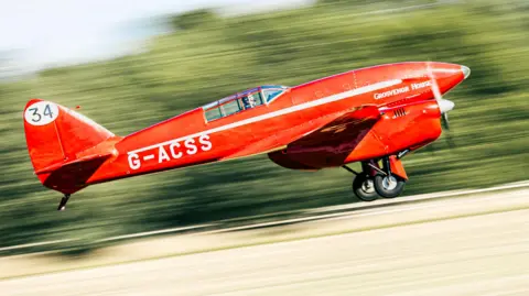 Sprite Photography The red DH.88 Comet is lifting off the ground with the background and ground blurred, illustrating the speed it is moving.