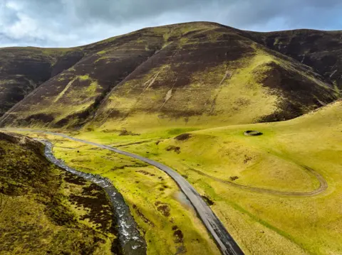 Getty Images The Mennock Pass in Dumfries and Galloway with a road beside a river next to a large hill