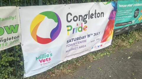 A white and rainbow coloured banner with the words Congleton Pride printed on it and details of the event on Saturday 19th July.