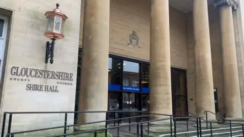 Carmelo Garcia The entrance to Shire Hall. There are four large pillars in front of the glass entrance doors. To the left is a copper street lamp.