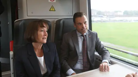 Welsh government Jo Stevens and Ken Skates sitting alongside each other on a train on Wednesday