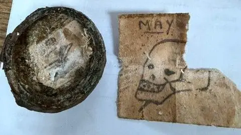 A picture of part of what Alex discovered. A round object is on the left of the picture whilst a note, hand-drawn with a skull, teeth and dagger in his head can be seen on the right. 