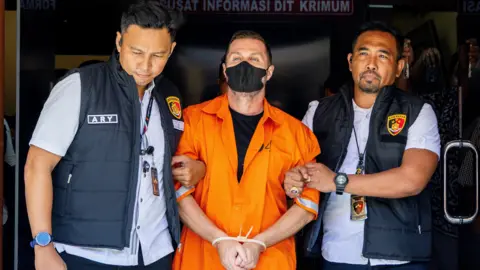 EPA Lyons has his hands tied together as he is led from the detention centre by two officers