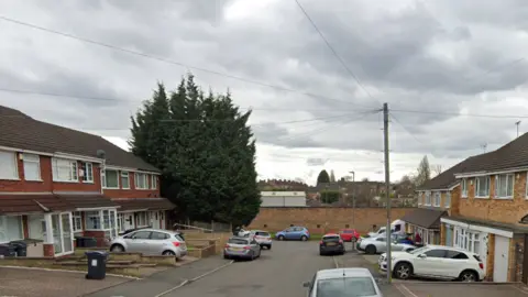 Houses can be seen on either side of the cul de sac with cars parked on drives and on the street