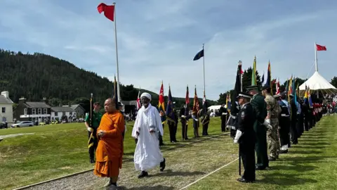 Two representatives walk down the ceremonial walkway while standard bearers line the walkway behind.