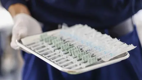 Getty Images A hand in a latex glove holds a tray of syringes filled with the Pfizer-BioNTech vaccine for Covid-19 at a vaccination centre in Munich, Germany, on Thursday, 2 Dec 2021