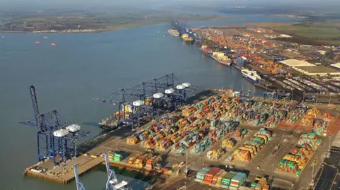 Mike Page Aerial Photography An aerial view of the Port of Felixstowe, showing cranes, containers stacked on the quays and half a dozen ships docked. In the background are is the village of Shotley Gate and the River Orwell.