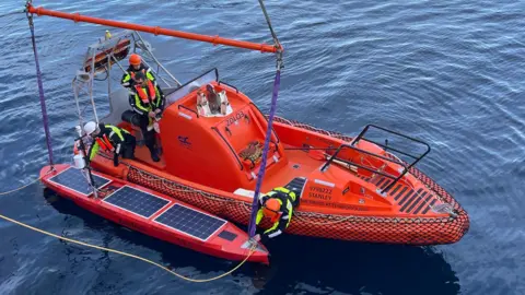 Carol Robinson/UEA Three people stood on a support boat and launching a surface vessel to collect samples