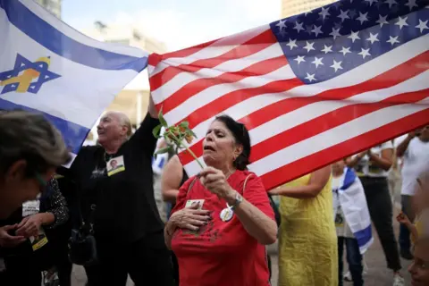 Agitando as bandeiras dos EUA e de Israel atrás das bandeiras da mulher da Reuters que está maravilhada com a flor parece estar dominada pela emoção