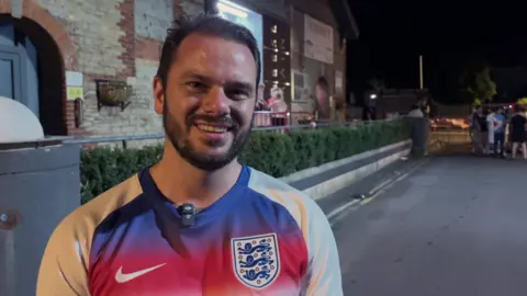 A man is pictured wearing an England football jersey on a street.