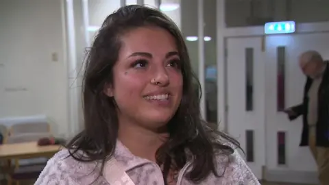 BBC Head and shoulders image of Tyler Winston at the meeting. She is smiling and has long brown hair