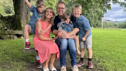 A family photo with a man and woman sitting on a swing and three children 