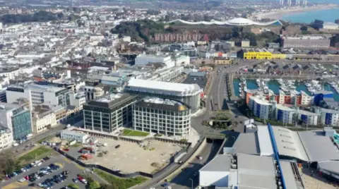 An aerial view of a large town with large buildings and roads and the sea beyond.