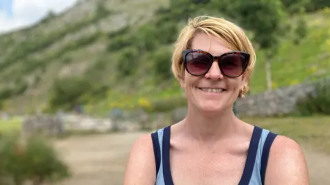 Woman with short blonde hair wearing sun glasses and a sleeveless blue top