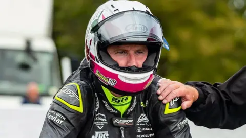 MANX GRAND PRIX Sam Naughton in his racing leathers and helmet on the start line with a hand on his shoulder.