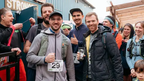 Kayleigh Bricknell @12kmedia A group of people who took part in the Ravers2Runners event in Bristol smile as they group together for the camera. Some of them have race numbers pinned to their torsos, and the group is made up of a variety of ages and contains both men and women