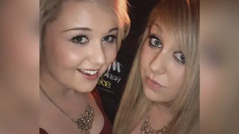 Family photo A selfie photo of two blonde girls wearing glitzy necklaces and low cut tops. They are both wearing lots of make up and smiling at the camera.