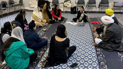 A group of people sit in a circle at a gurdwara