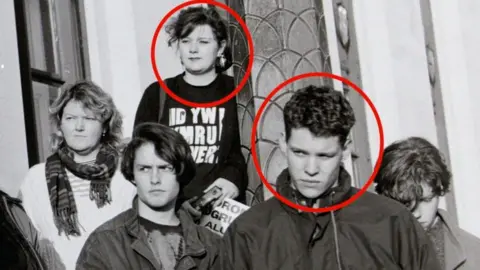 Chris Reynolds This image is a cropped version of the first photograph. It shows a young Leanne Wood stood behind Rhun ap Iorwerth. She is wearing a t-shirt that reads 'Wales is not for sale' in Welsh.