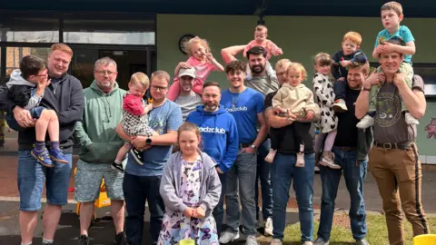 Fathers and children stand together outside in a sunny garden in Portsmouth